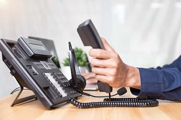 Close-up of hands using a desk telephone and headset in an office setting, highlighting grenke's financing options for phone systems, VoIP technology, and communication solutions to ensure smooth business operations.